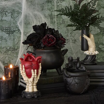 Black pot with dark colored roses and a pot in the shape of skeleton hands grabbing a red heart.