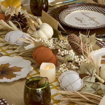Warm autumn tablescape with white pumpkins, dried leaves, berries, pinecones, patterned plates, green glassware, and a glowing candle.