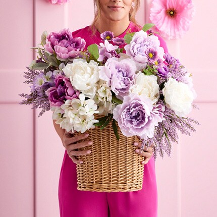 woman in pink holding wicker basket filled with white and purple flowers 