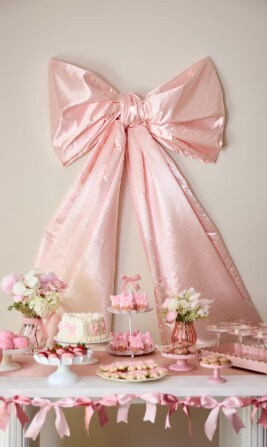 large pink bow on wall behind table of cakes for wedding shower