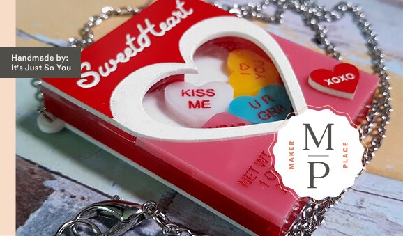 MakerPlace by Michaels A heart-shaped pendant mimicking a candy box reads "Sweet Hearts" with colorful candies inside. Chain attached, with a small "XOXO" token. Emotive and playful.