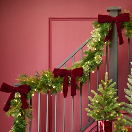 Christmas Garland greenery with large velvet burgundy bows on a stair case
