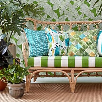 patio love seat with green and white striped cushion and tropical pillows next to plants