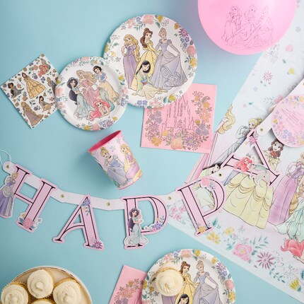 A princess-themed party table with pink decor, cupcakes topped with princess toppers, pink forks, and plates featuring animated princess characters.