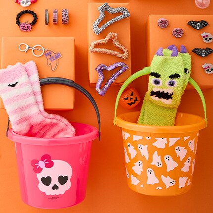 Two buckets: one pink with a skull and the other one orange with white ghosts. Toys and accessories surrounding. 