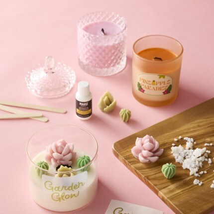 3 candles with candle making supplies on pink background 