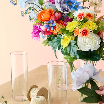 Floral arrangement setup featuring a variety of colorful artificial flowers in a clear vase on a beige surface. 