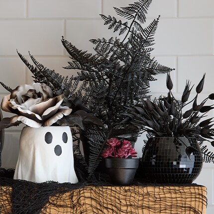 Black Floral Stems in black pots over a tabletop next to a ghost tabletop decoration.