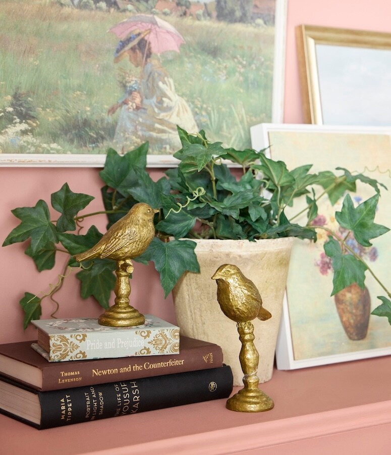 gold bird statues with ivy plant and stacked books on shelf