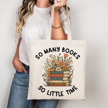 MakerPlace by Michaels A person holds a tote bag with the text "So Many Books So Little Time." The bag features a colorful illustration of stacked books and flowers, conveying a love for reading.