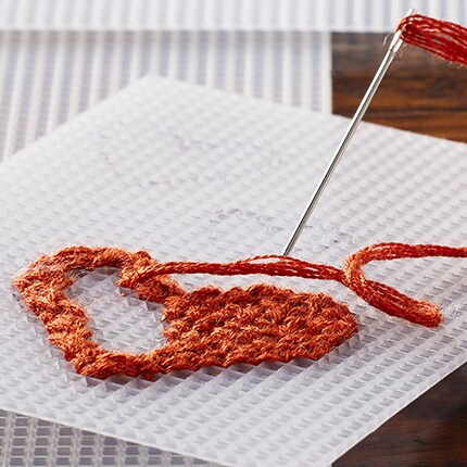 needle with orange yarn making heart shaped cross stitch