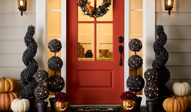 Front porch decorated for Halloween with a red door, black spiral topiary lights, and various pumpkins in white, orange, and metallic colors. 