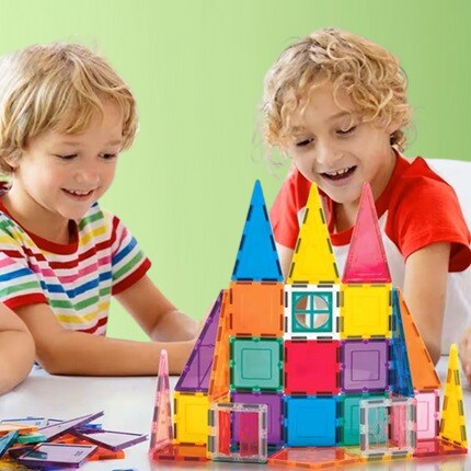two blonde boys stacking magnetic tiles on table