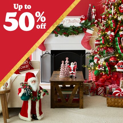 red room with santa and stockings on mantle, with decorated Christmas tree and wood table with ceramic tree accents with 50% off in white text in red triangle