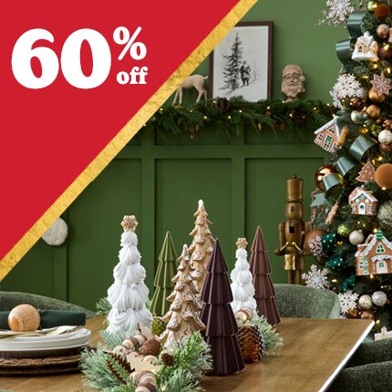 green room with reindeer and stockings on wall, with decorated Christmas tree and wood table with ceramic tree accents with 60% off in white text in red triangle