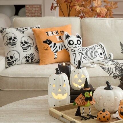 Halloween themed pillows in orange, white and black colors in a couch and white decor pumpkins in a center table.