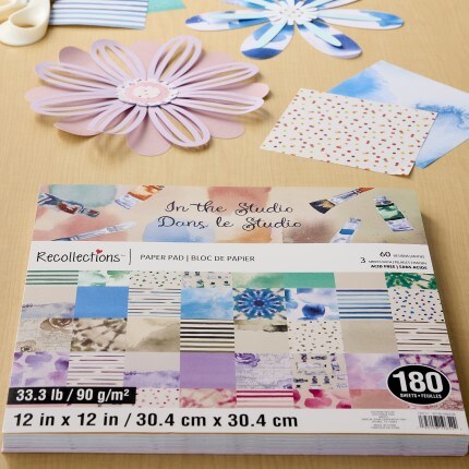 assorted stack of recollections in the studio themed scrapbook paper pad with pink and blue paper flowers all sitting on a wooden table 