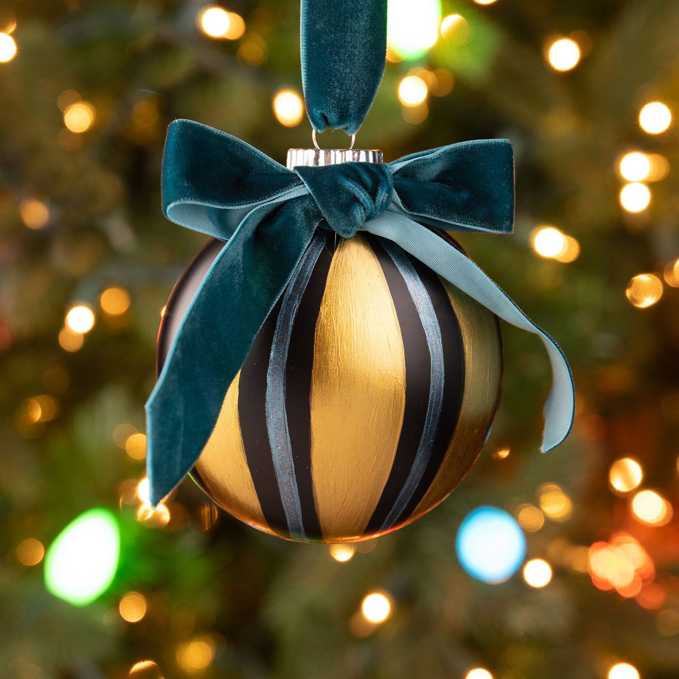 A gold ornament with painted stripes and dark velvet ribbon