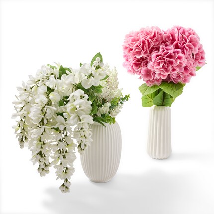 Two white ceramic vases containing floral arrangements against a white background.
